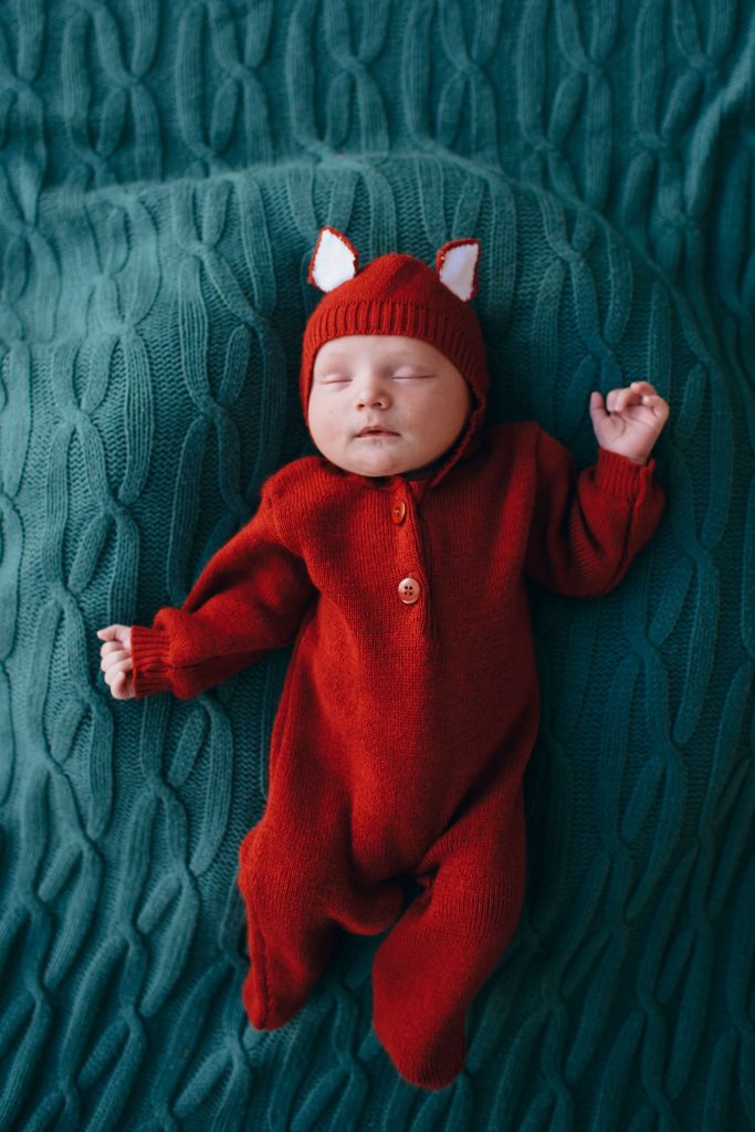 Print on demand baby clothes - Baby on a bed wearing a red fox long sleeve onesie