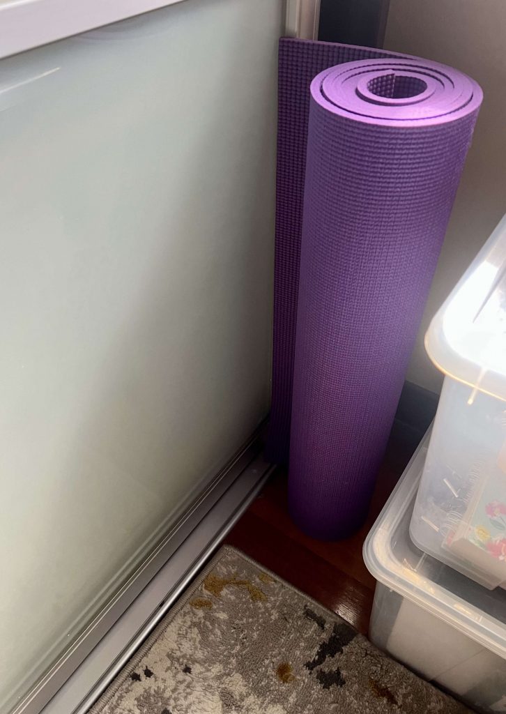 purple yoga mat rolled up in corner of a room